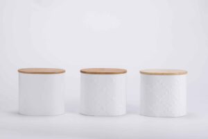 White metal tea coffee sugar canisters with bamboo lids arranged on a kitchen counter.
